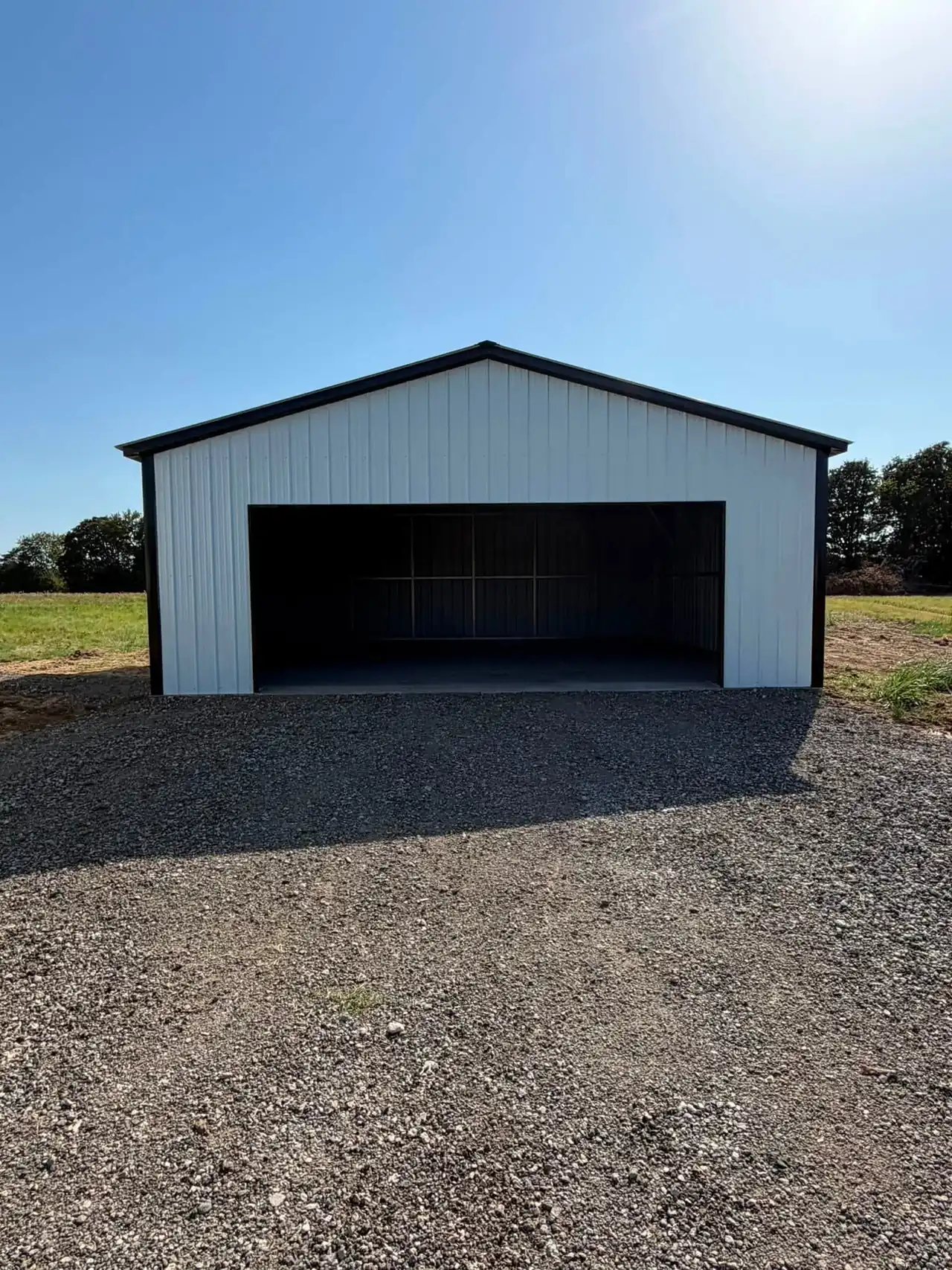 White metal garage with a black roll-up door on a gravel pad
