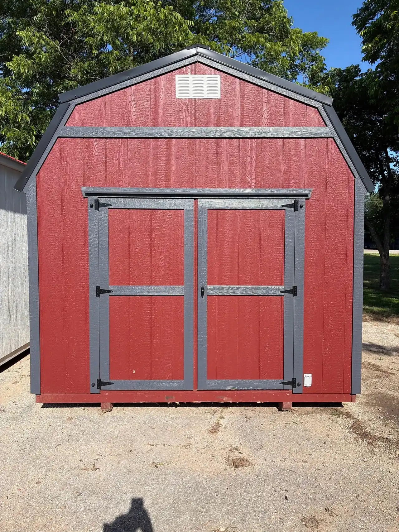 Red lofted barn with gray trim and double doors on gravel