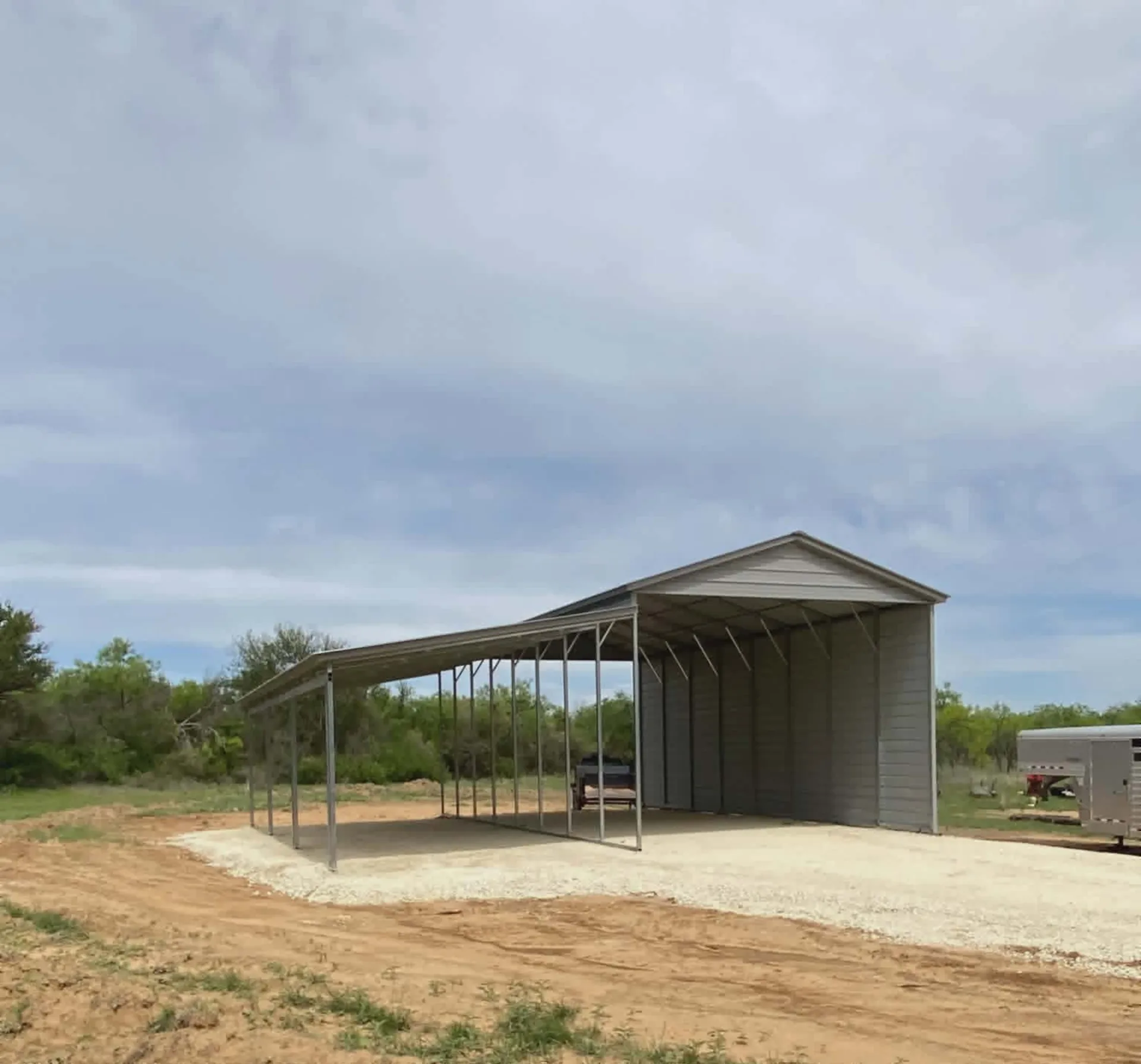Open metal carport with a long roof on a gravel pad