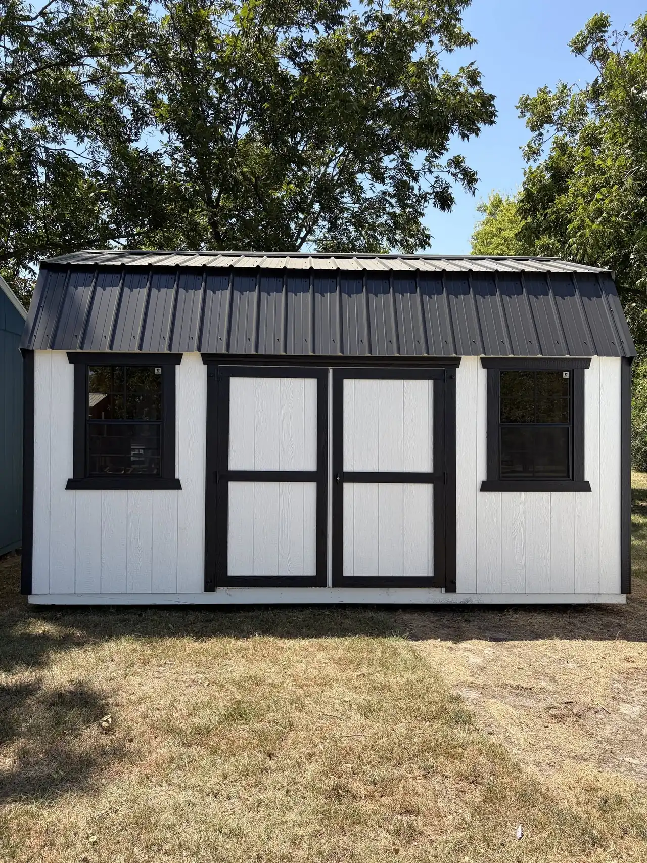 White portable building with black trim, a black metal roof and double doors
